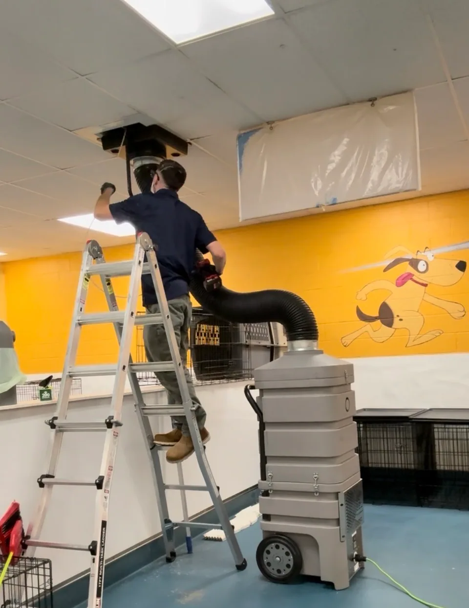 Technician cleaning a ceiling air duct with a large vacuum hose