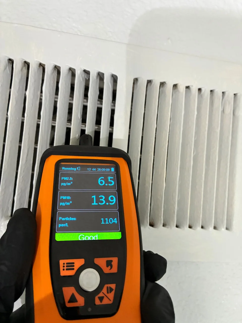 Handheld particle meter taking a reading at an air vent